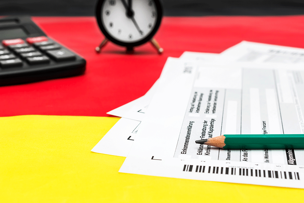 Nemecký daňový formulár s kalkulačkou na vlajke. Preklad: daňové priznanie k dani z príjmov, príjmy z kapitálového majetku, žiadosť o zamestnanecké úspory, prenesenie daňovej straty, daňové číslo, daňový úrad, zmena bydliska, všeobecné informácie, zdaniteľná osoba.