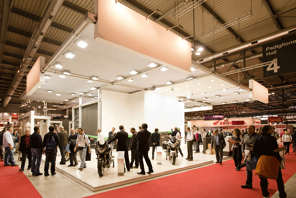 Návštevníci a vystavovatelia komunikujú pri stánkoch na medzinárodnom veľtrhu v modernej výstavnej hale.