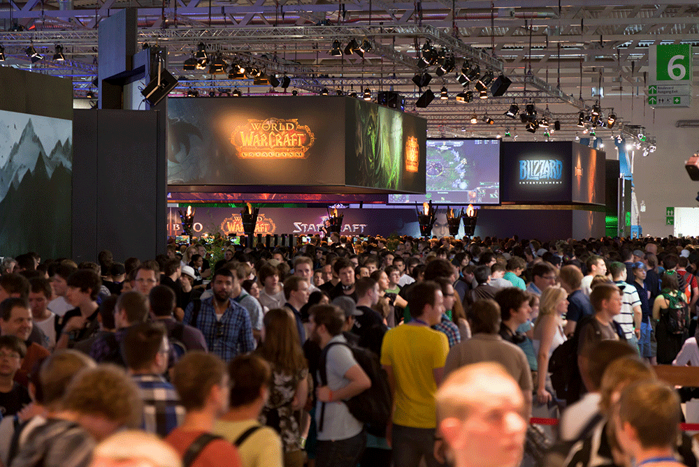 Dav návštevníkov na veľtrhu Gamescom 2011 v Kolíne nad Rýnom, pod veľkoplošnými obrazovkami a stánkami vystavovateľov z videoherného priemyslu.