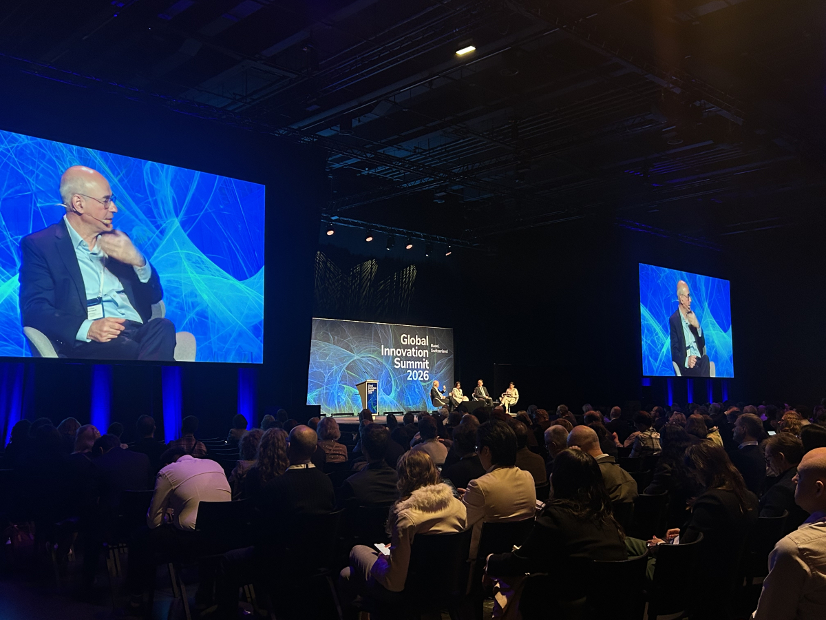 Publikum sleduje panelovú diskusiu na podujatí Global Innovation Summit 2026 v Bazileji. Na pódiu sú rečníci a za nimi veľkoplošné obrazovky s vizuálom summitu a detailom jedného z diskutujúcich.